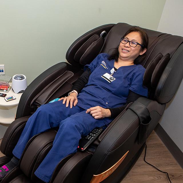 Melanie Mallari, wearing blue scrubs, sits in a black massage chair