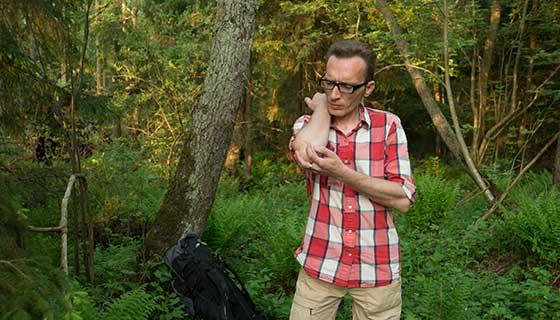 A man scratches at a mosquito bite in the woods.