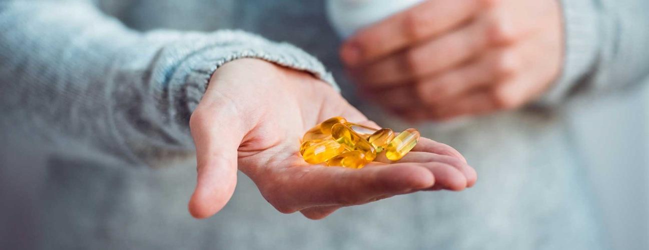 A person holds a handful of vitamins in their hand.