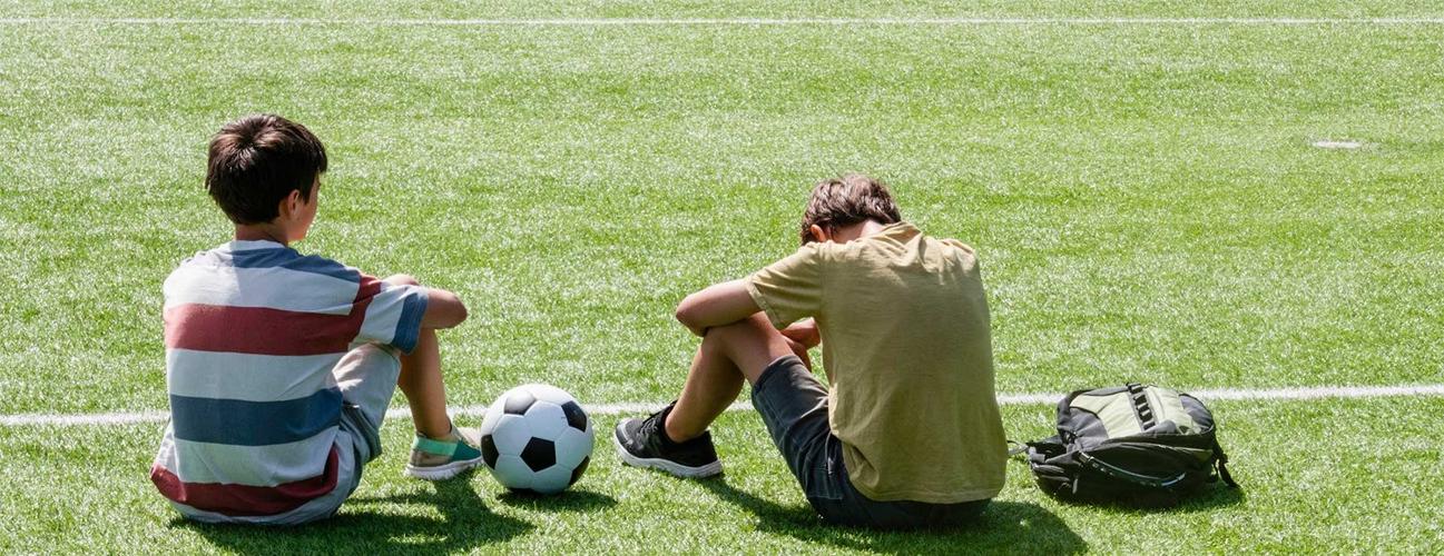 两个学生运动员坐在足球场上，一个低着头.