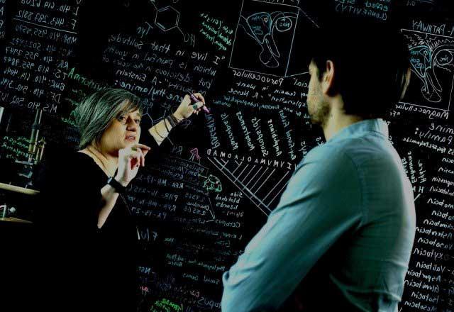 Researcher writing on a blackboard with chalk and talking to a colleague. 